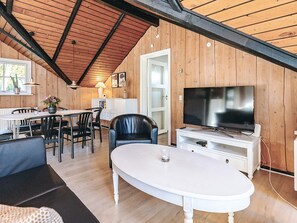 A cozy living room with a white sofa, a dining table with chairs, a TV on a white stand, and wooden walls. - Alluring Holiday Home in Falster near Sea (Vaeggerlose)