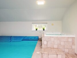 A swimming pool with a blue deck, a hot tub, and a window with plants.