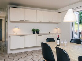 A modern kitchen with white cabinets, a dining table with chairs, and a hanging light fixture.