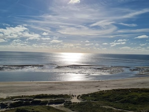 A beach with a clear sky, calm sea, and distant wind turbines.
