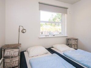 A bedroom with two beds, a window with a view, a lamp, and a small table.