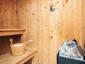 Una sauna de madera con un banco de madera, un cubo de madera y un recipiente metálico con piedras.