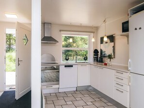 A compact kitchen with white cabinets, a built-in oven, a dishwasher, and a window with a view of greenery.