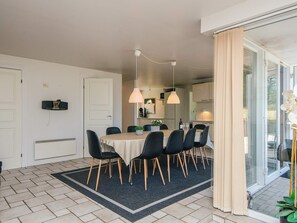 A dining area with a table set for four, chairs, a rug, pendant lights, and a sliding glass door leading to a balcony.