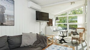 A living room with a sofa, a coffee table with a blue and white pattern, a television, a computer, and a wicker chair. - Modern Holiday Home With Large Terrace in Fanø (Fano)