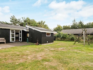 A black building with a white door and windows, a bench, and a swing set in a grassy yard. - Modern Holiday Home With Large Terrace in Fanø (Fano)