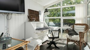 A room with a large window, a television, a desk with a chair, and a wicker chair. - Modern Holiday Home With Large Terrace in Fanø (Fano)