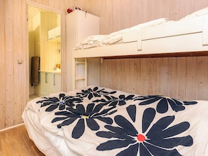 A bunk bed with a floral bedspread, a wooden wardrobe, and a bathroom with a towel hanging.