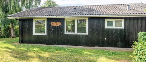 A black wooden building with a tiled roof, a sign reading 'Mon Ami,' and a grassy yard.