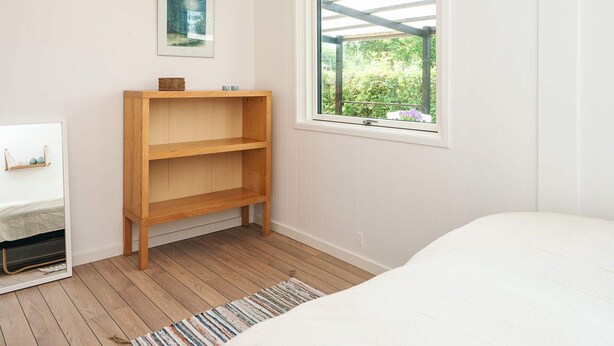 A bedroom with a bed, a wooden shelf, a framed picture, and a window with a view of greenery. - 4 Person Holiday Home in Juelsminde (Horsens)
