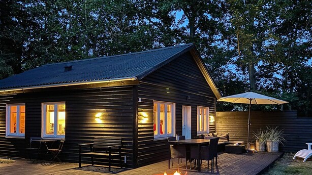 En træhytte med terrasse, udendørs møbler og bålsted.