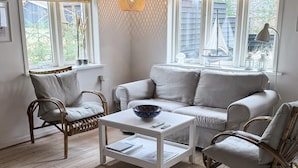 En hyggelig stue med en sofa, to fletstole, et sofabord og en hængende lampe.