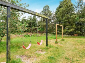 A wooden swing set in a grassy area with trees in the background.