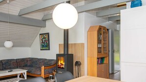 A modern interior with a sofa, a dining table with potted plants, a wooden cabinet, and a black wood-burning stove. - 6 Person Holiday Home in Romo (Rømø)