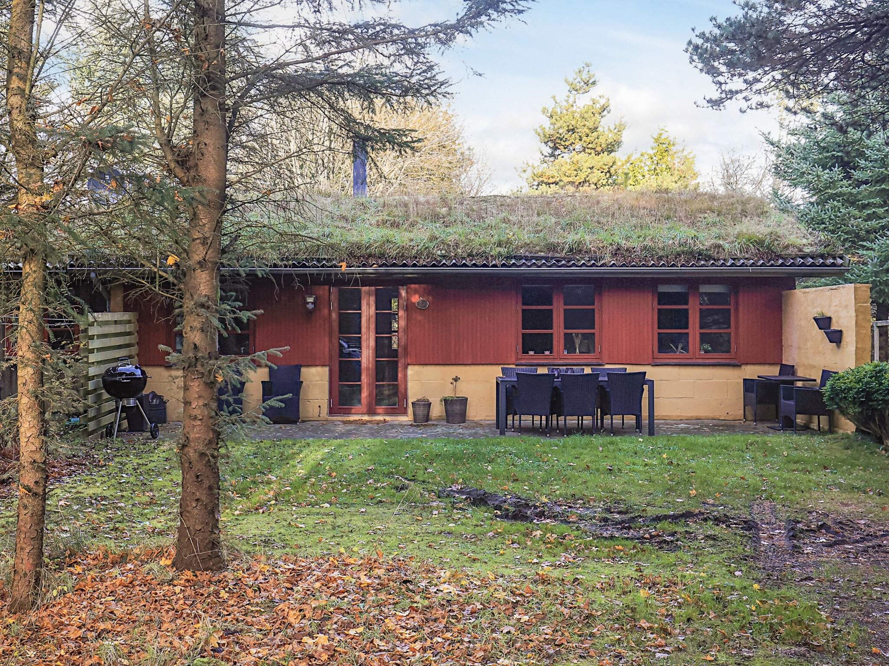 Une maison à l’extérieur rouge, dotée d’une terrasse en bois et d’un barbecue.