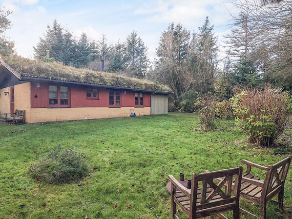 A house with a sloped roof, a small shed, and a grassy yard with a bench.