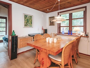 A dining area with a wooden table, wicker chairs, and a window with a view of trees.