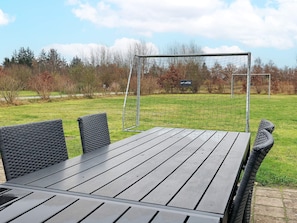 An outdoor dining area with a table and chairs, a swing set, and a grassy field with trees in the background. - 5 Star Holiday Home in Hojslev (Hojslev)
