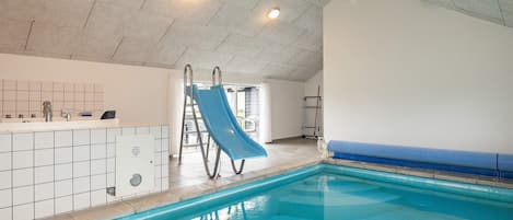 An indoor swimming pool with a slide, a changing room, and a shower area.
