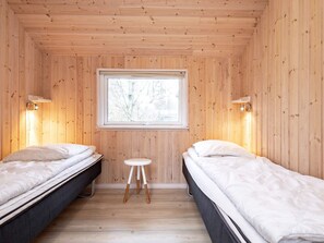 A small, wooden-paneled room with two single beds, a small stool, and a window with a view of trees.