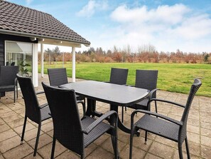 Une terrasse avec une table et des chaises, un espace salon abrité et une vue sur un champ verdoyant.