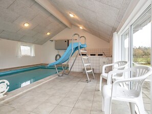 An indoor swimming pool with a blue slide, a ladder, and white plastic chairs.