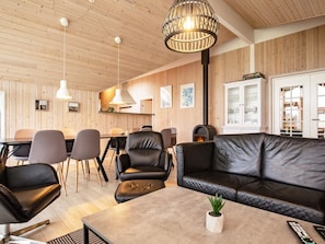Un interior moderno con techo de madera, un sofá de cuero negro, un comedor con sillas y una chimenea.