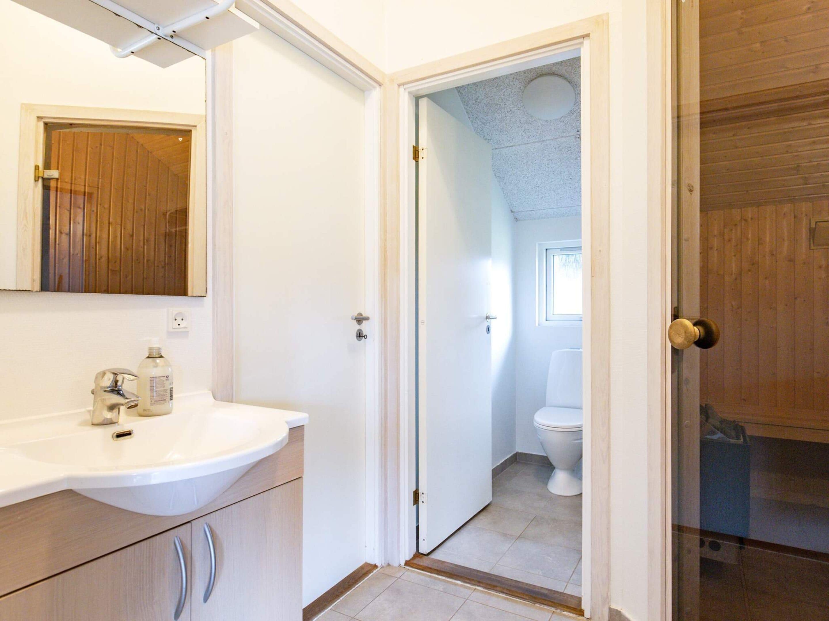 Un baño con lavamanos, espejo e inodoro blancos.