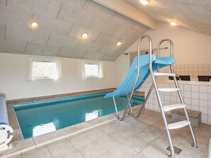 An indoor swimming pool with a blue slide, a ladder, and two windows. - 5 Star Holiday Home in Hojslev (Hojslev)