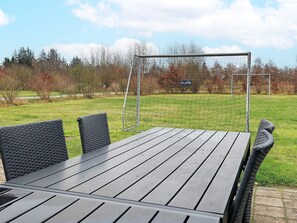 A wooden table with four chairs, a swing set, and a grassy field with trees in the background. - 5 Star Holiday Home in Hojslev (Hojslev)
