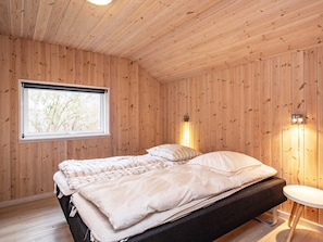 A wooden-paneled room with a bed, a window, and wall-mounted lighting.