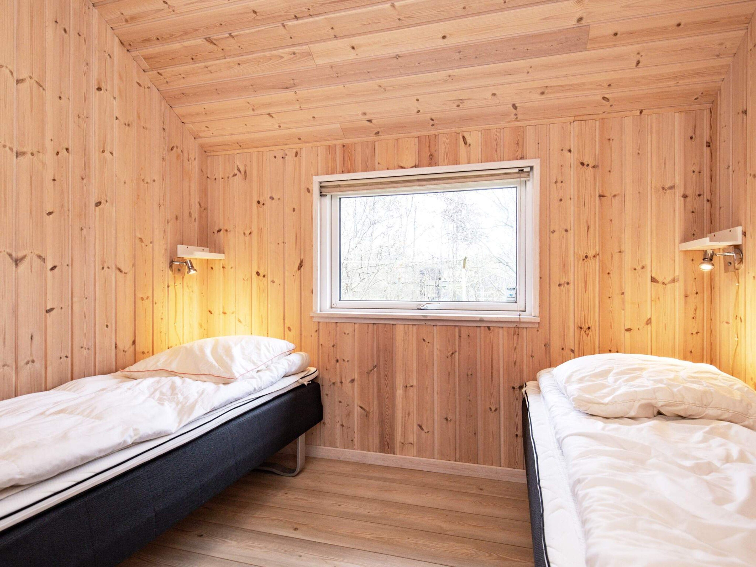 A room with two beds, wooden walls, a window, and wall-mounted lights.
