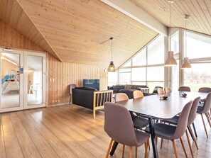 A spacious room with a wooden ceiling, large windows, a dining table with chairs, a sofa, and a television. - 5 Star Holiday Home in Hojslev (Hojslev)