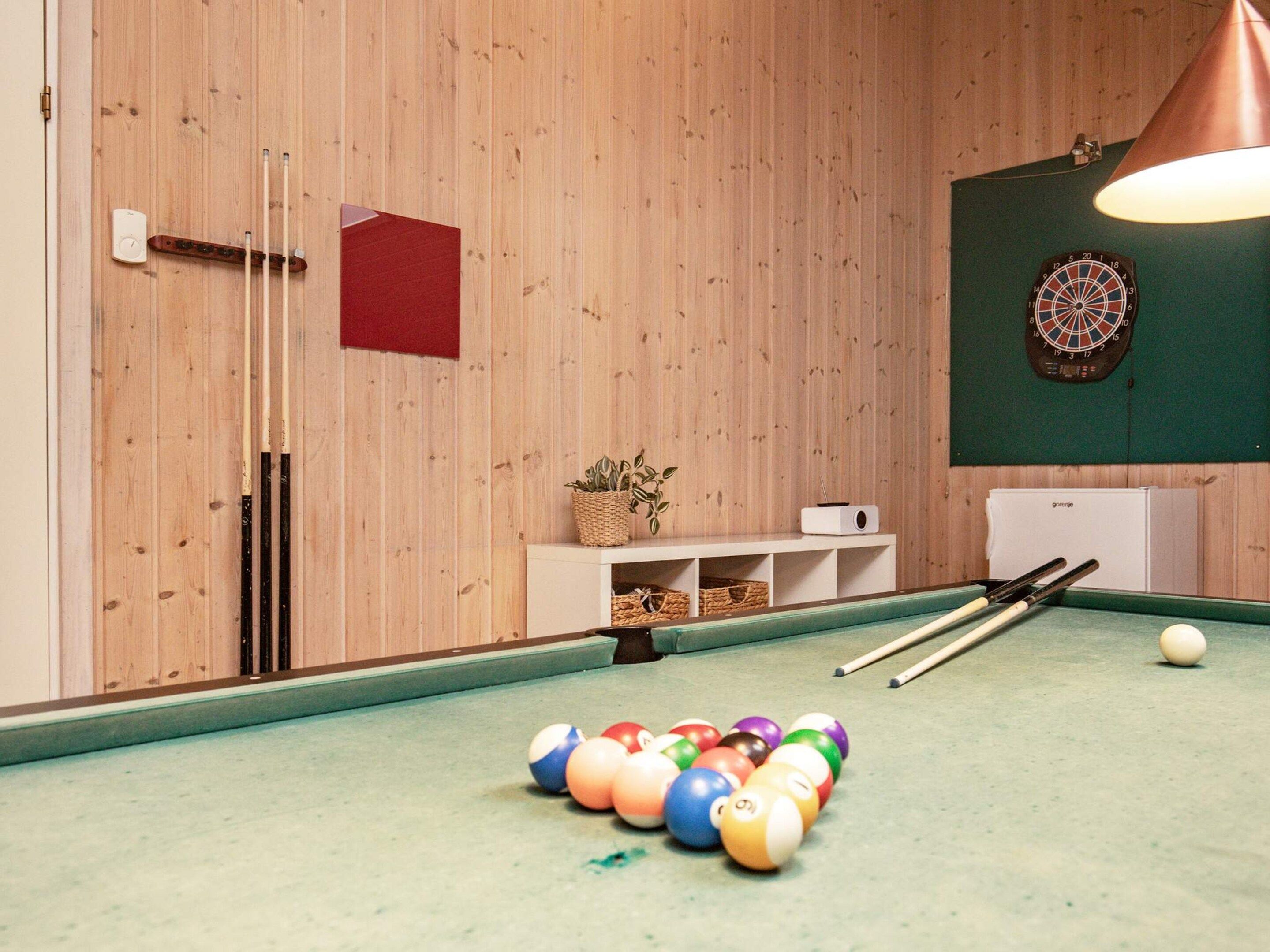 A billiards table with balls and cues, a dartboard, and a small shelf with a plant and a radio.