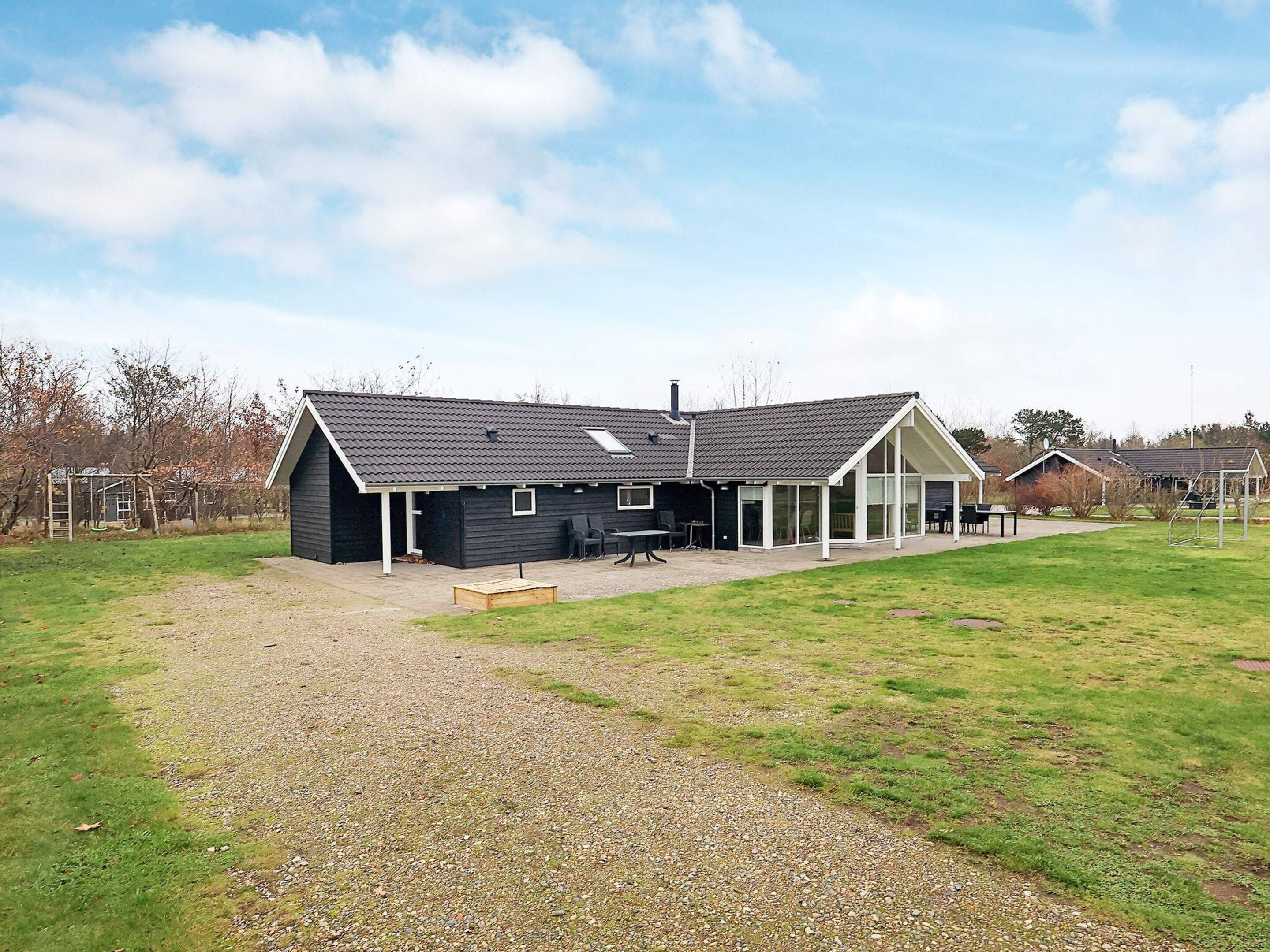 A modern house with a patio area, a covered outdoor seating space, and a gravel driveway.