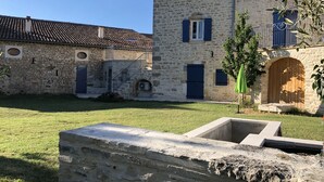 A stone building with a tiled roof, a wooden door, and a small garden area. - Gîte Léonie "Between Cèze and Ardèche" 30430 BARJAC (Barjac)