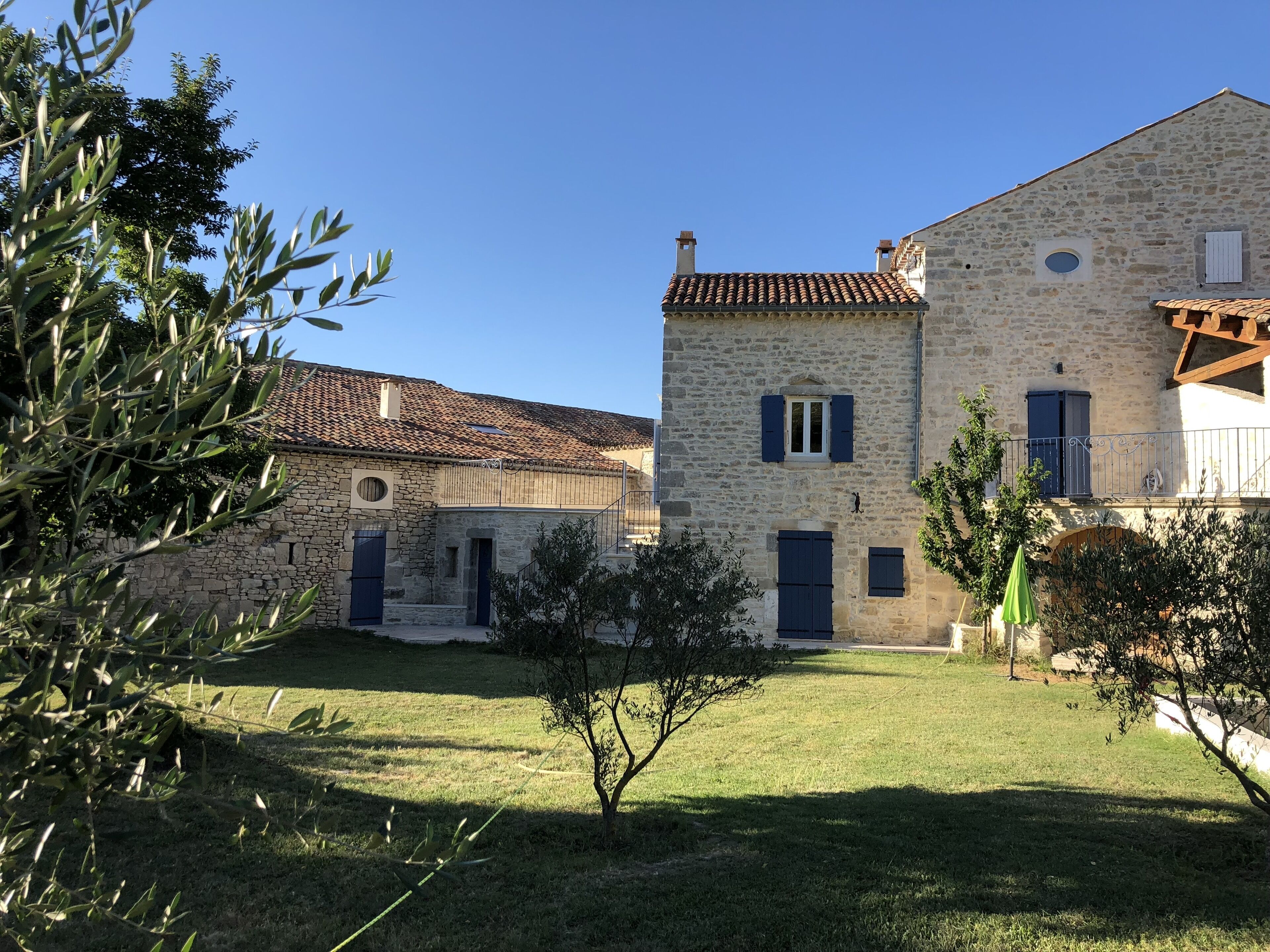 A stone building with a tiled roof, a small garden, and a tree with olive branches.