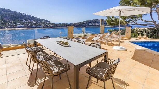 Una terraza con piscina, zona de comedor y vistas al mar.