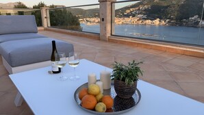 Una terraza con una mesa blanca, una botella de vino, copas, velas y un frutero.