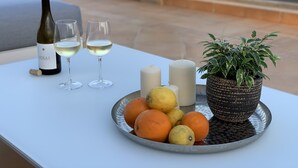 Una mesa con una botella de vino, dos copas, velas, una planta en maceta y una bandeja de frutas.