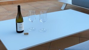 Una botella de vino y dos copas sobre una mesa blanca, con vista al mar.