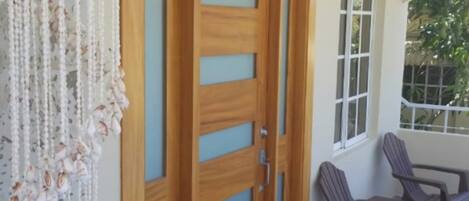 Uma porta de madeira com painéis de vidro, uma decoração de macramé pendurada e uma área de pátio com cadeiras e uma mesa.