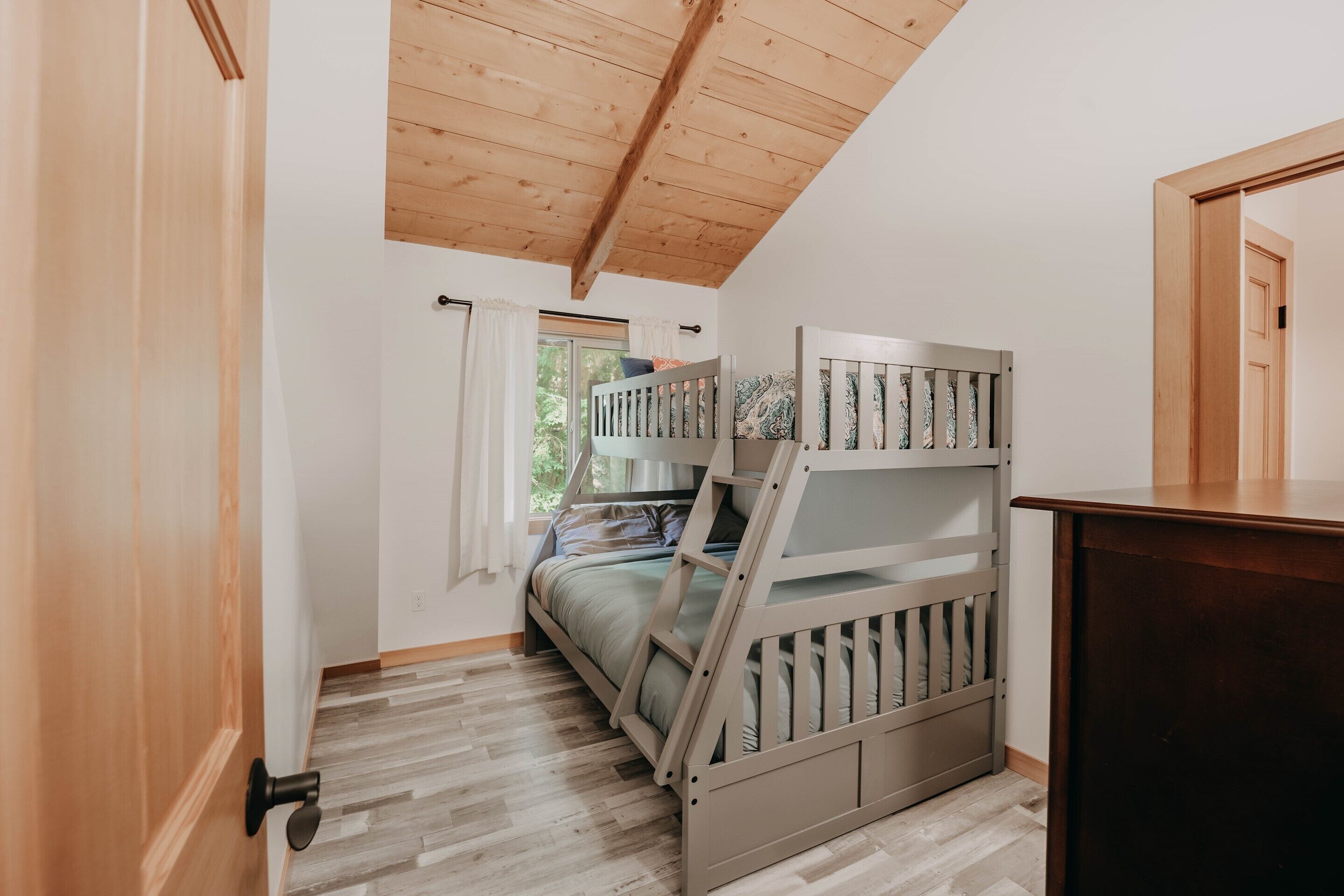 Une chambre avec un lit superposé, un plancher en bois, une fenêtre avec des rideaux et une porte.