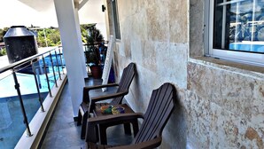 Un balcon avec deux chaises en bois et une table, une piscine et un barbecue.