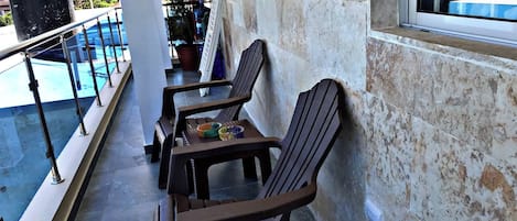 A balcony with two wooden chairs and a table, a pool, and a grill.