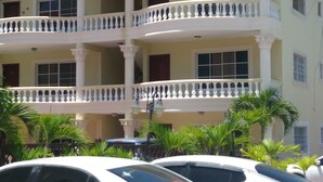 A multi-story building with balconies, columns, and a parking area with cars. - Room-room With fan use Bavaro Punta Cana (Punta Cana)