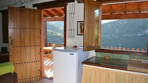 Uma cozinha com porta de madeira, geladeira, janela com vista para montanhas e luminária pendente.