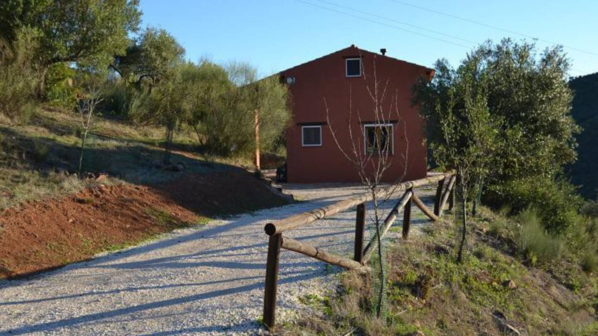 A red building with a gravel driveway and wooden fence.