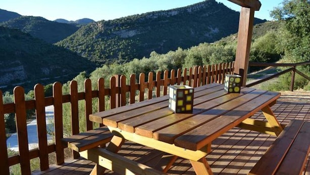 Mesa de piquenique de madeira com bancos e cerca de madeira, com montanhas ao fundo.