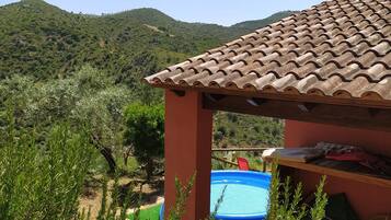 Un espacio exterior rústico con techo de tejas, una piscina azul y una terraza de madera.